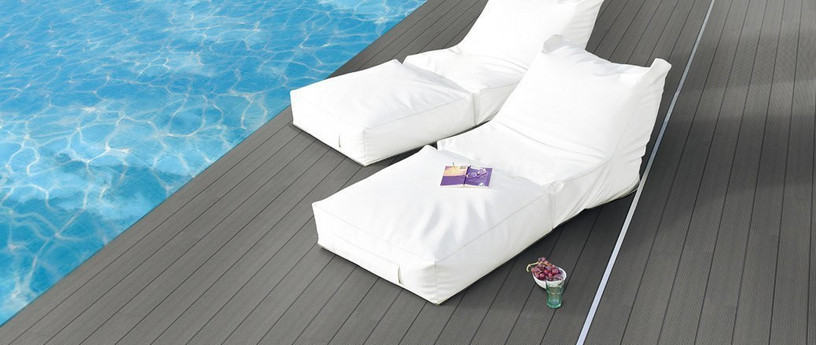 Elegante Poolterrasse mit dunklem WPC-Belag, zwei weißen Lounge-Liegen und ruhiger Wasserreflexion.