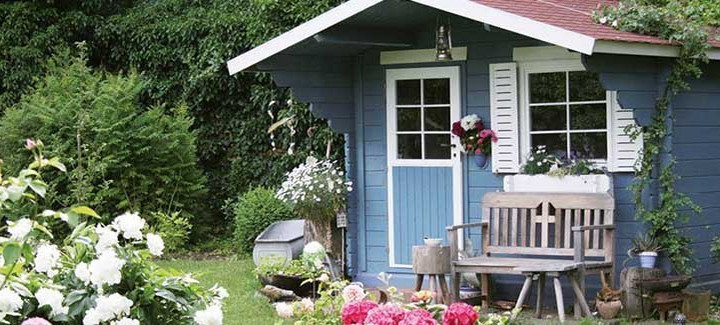 Ein blau-weißes Gartenhaus aus Holz in einem schönen Garten