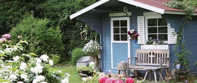 Ein blau-weißes Gartenhaus aus Holz in einem schönen Garten