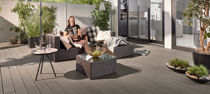 Moderne WPC-Terrasse mit anthrazitfarbenem Sichtschutzzaun, Loungemöbeln und Sonnenschirm.